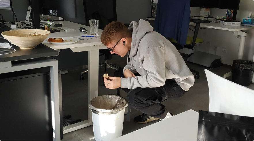 Young man squatting by a trash bin in an office